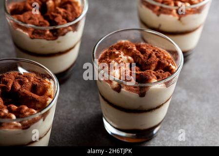 Köstliche traditionelle Tiramisu-Wüste in kleinen Glasbechern auf steinerner Arbeitsplatte serviert. Das Bild bei schwachem Licht zeigt Textur und Schichten aus dem Winkel mit flacher Oberfläche Stockfoto