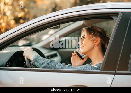 Foto von Junge schöne blonde Frau fährt Auto, verstößt gegen Verkehrsregeln, wird abgelenkt, schaut auf den Bildschirm des Mobiltelefons, nutzt Smartphone, schnelles Tempo Stockfoto