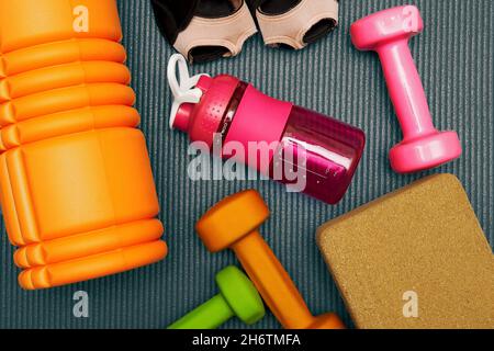 Getönte flache Lay-Schablone mit Fitnessgeräten, Hantel, Roller, Flasche auf der Matte. Gym Eqip und Gesundheitswesen Hintergründe Stockfoto