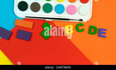 Eine Palette von Aquarellfarben, Alphabeten und Formen auf farbigem Hintergrund. Selektiver Fokus auf das Alphabet. Stockfoto