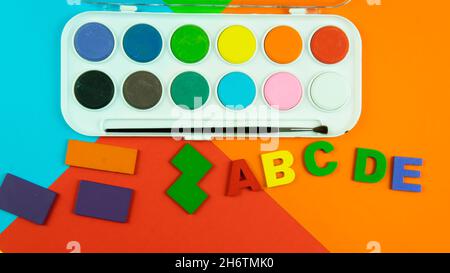 Eine Palette von Aquarellfarben, Alphabeten und Formen auf farbigem Hintergrund. Selektiver Fokus auf das Alphabet. Stockfoto