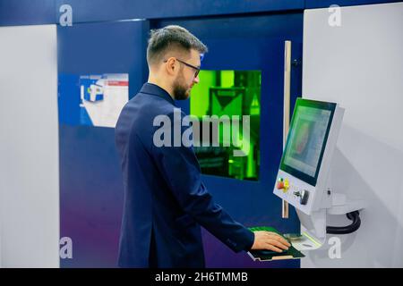 Industriearbeiter Mann in Gläsern, die CNC-Laser-Drehmaschine auf automatischem modernen Fabrikboden bedienen. Stockfoto