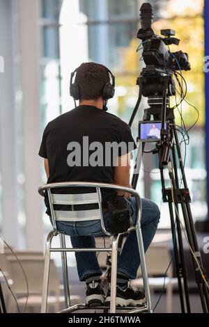 Camcorder Operator filmt Live-Show auf einem Stuhl sitzend. Stockfoto