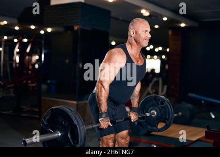 Glatze Sportler im Alter, die Gewichte heben, trainieren im Fitnessstudio und trainieren mit der Langhantel die Rückenmuskulatur Stockfoto