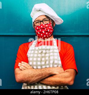 Konzept der Arbeiter, die eine Maske für Covid-19-Coronavirus-Einschränkungen und den Ausbruch von Ansteckungen tragen. Mann Restaurant Koch mit roter Schutzmaske und c Stockfoto