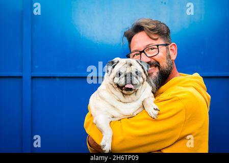 Fröhliches Porträt eines erwachsenen Mannes und seines schönen alten Moorhundes zusammen vor einem blauen Wandhintergrund. Konzept von Glück und besten Freunden Menschen und ein Stockfoto