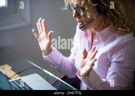 Erwachsene Frau, die im Büro mit modernen Online-Aktivitäten beschäftigt ist, und Kopfhörer und Laptop-Computer verwendet, um zu sprechen und mit einem entfernten Team zu kommunizieren. Konzept von int Stockfoto