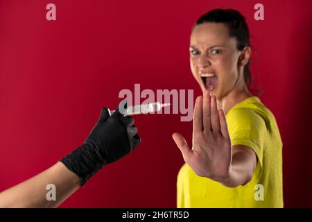 Die Frau weigert sich, den Impfstoff auf rotem Hintergrund zu erhalten Stockfoto