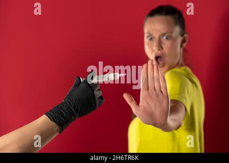 Die Frau weigert sich, den Impfstoff auf rotem Hintergrund zu erhalten Stockfoto