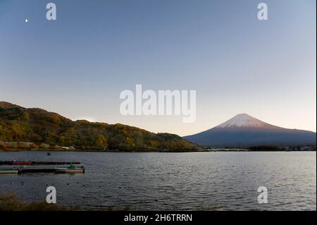 Mount Fuji vom Kawaguchiko-See in der Präfektur Yamanashi aus gesehen, mit dem Mond bei Sonnenuntergang. Stockfoto