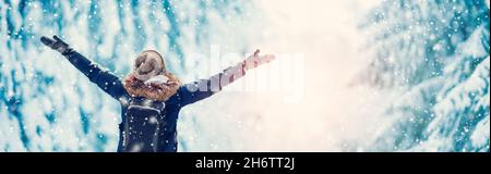 Glückliche Frau mit hochstehenden Händen im verschneiten Wald bei Schneefall. Stockfoto