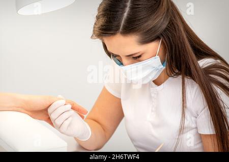 Manikurist trägt Schutzmaske Malerei weibliche Nägel mit Nagellack in Maniküre Salon Stockfoto