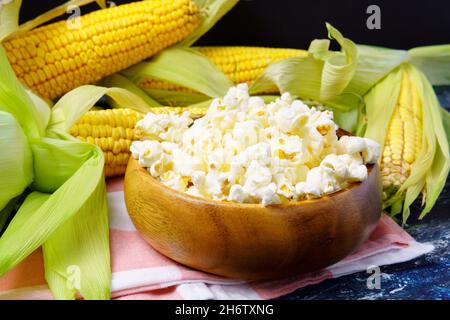 Leckeres Popcorn in einer Schüssel auf dem Tisch. Ähren von frischem Mais auf dunklem Hintergrund Stockfoto