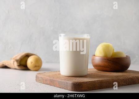 Vegane Kartoffelmilch im Glas und Kartoffel in Schüssel auf hellem Hintergrund. Nahaufnahme. Milchaustauschstoff auf pflanzlicher Basis und laktosefrei. Stockfoto