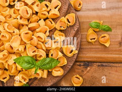 Tortellini auf einem Holzbrett mit Basilikum und Parmesan. Spezialitäten der Küche aus Bologna und der Emilia Romagna: Cappelletti, frische Eiernudeln mit Fleisch- und Gemüsefüllung Stockfoto
