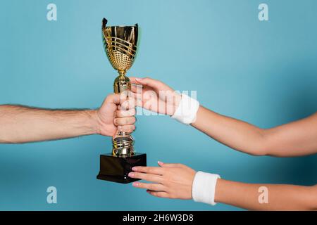 Beschnittene Ansicht des Mannes, der eine goldene Trophäe an die weibliche Meisterin auf Blau überreicht Stockfoto