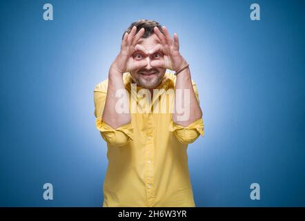 Dumme Kerl starrte zu Ihnen über blauem Hintergrund, Kleider in gelbem Hemd. Halber Länge lustige junge Mann. Joke-Konzept. Studioaufnahme Stockfoto