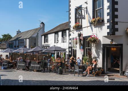 Pub UK, im Sommer können Sie sich an Tischen vor dem beliebten Dog and Gun Pub im Zentrum von Keswick, Lake District, Cumbria, England, entspannen Stockfoto