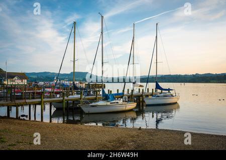 Waterhead, Blick an einem Sommerabend auf Boote, die entlang der Anlegestelle in Waterhead, einem Hafen am Nordufer des Lake Windermere, Cumbria, England, festgemacht sind Stockfoto