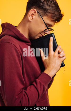 Der Christ betet mit geschlossenen Augen mit einer Bibel in seinen Händen. Der Mensch betet auf der Heiligen Bibel, die Hände gefaltet im Gebet auf der Heiligen Bibel auf einer gelben Straße Stockfoto