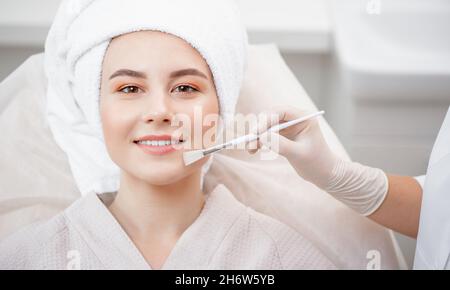 Arzt wendet Lifting-Creme oder Clearing Akne Haut mit Pinsel der jungen Frau im Schönheitssalon. Stockfoto