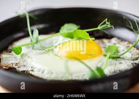 Servieren von Spiegeleiern in gusseisernen Pfanne mikrogrünen Sprossen Baby Bohnen Erbse und Sonnenblume auf weißem Hintergrund. Stockfoto