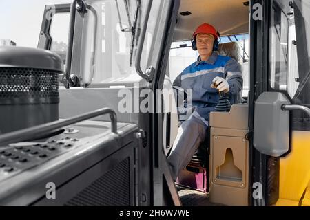 Glücklicher Fahrer Mann von industriellen Muldenkipper sitzt in der Kabine und arbeitet auf der Baustelle. Stockfoto