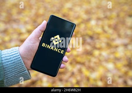Binance App-Logo auf dem Smartphone in der Hand einer Frau mit verwackelten gelben Herbstlaub Hintergrund. Kryptowährungsbörse, Handelsplattform. Warschau, Polen - 19. Oktober 2021 Stockfoto