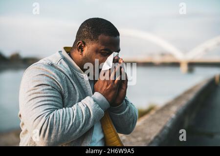Schwarzer Mann bläst die Nase, während er draußen sitzt. Stockfoto