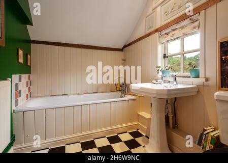 Hargrave, Suffolk, England - Juni 10 2020: Kleines Cottage-Badezimmer in traditionellem britischen Haus mit kompakter Badewanne und bemalten Holzpaneelen. Stockfoto