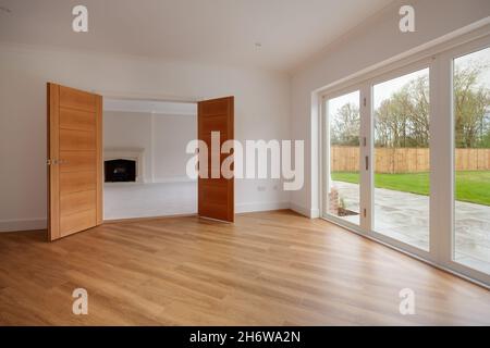 Clavering, England - April 6 2020: Großer Speisesaal in nagelneuem Haus mit weiß gestrichenen Wänden, Holzboden und doppelt öffnenden Türen Stockfoto