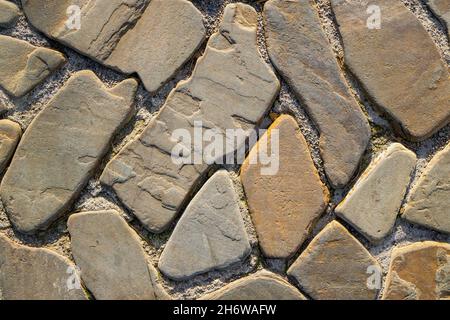 Flache ovale Steine in Zementbodenfliesen. Von oben aufgenommen. Pflasterstein Hintergrund. Das Pflaster besteht aus Natursteinen mit abgerundeter Form. Flach liegend. Stockfoto