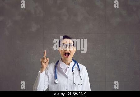 Ärztin im Laborkittel, die mit erhobenem Zeigefinger nach oben zeigt Stockfoto