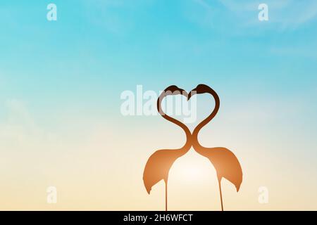 Silhouette von Flamingo in Herzform auf Grasfeld bei Sonnenuntergang Hintergrund. Stockfoto