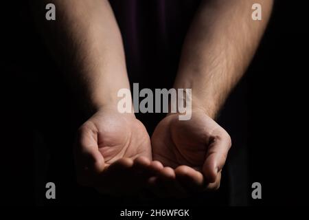 Männliche Hände, die Handflächen im Dunkeln nach oben. Fragen, Gebetskonzept. Stockfoto