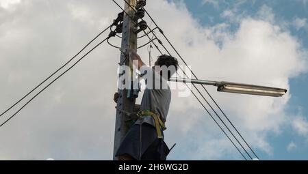 Elektriker, Mechaniker klettern und arbeiten an elektrischen Masten. Konzept der falschen Arbeitsweise und keine Sicherheit kein Helm. Stockfoto