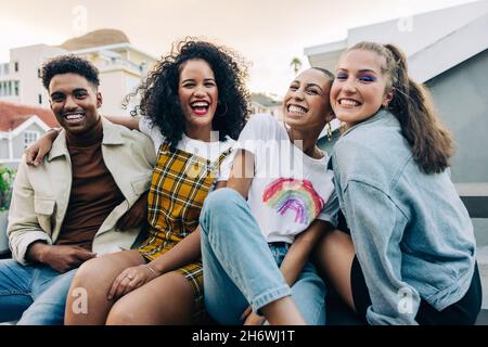 Freunde lächeln auf die Kamera, während sie auf einem Dach sitzen. Eine Gruppe fröhlicher junger Freunde, die am Wochenende gerne zusammen rumhängen. Vier Happy fr Stockfoto