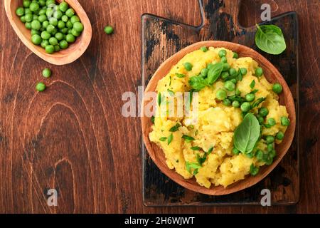 Kartoffelpüree mit Butter, grünen Erbsen, Zwiebeln, Basilikum auf rustikalem Holzhintergrund. Draufsicht mit Nahaufnahme. Stockfoto