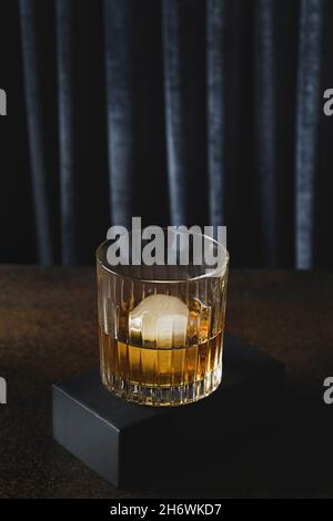 Kalter Whiskey mit Eis oder Brandy in altem Fasion-Rock-Glas auf dunklem, modernem Hintergrund mit Podium. Stockfoto