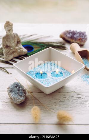 Blaue und weiße granulierte Wachskristalle, um Kerzen zu erzeugen, indem man in die Schüssel gießt und Docht einführt. Handgemachte Sandkerze in weißer Keramikschale auf Weiß. Stockfoto