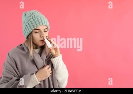 Junge Frau mit Nasenspray auf rosa Hintergrund, laufende Nase Konzept Stockfoto