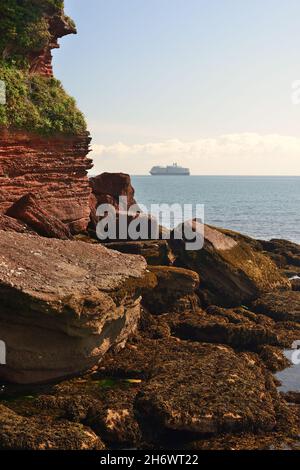 Felsen am Ende von Roundham Head, Goodrington, South Devon, mit einem Schiff, das während der Coronavirus-Pandemie vor der Küste vor Anker liegt. Stockfoto