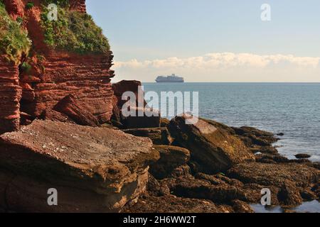 Felsen am Ende von Roundham Head, Goodrington, South Devon, mit einem Schiff, das während der Coronavirus-Pandemie vor der Küste vor Anker liegt. Stockfoto