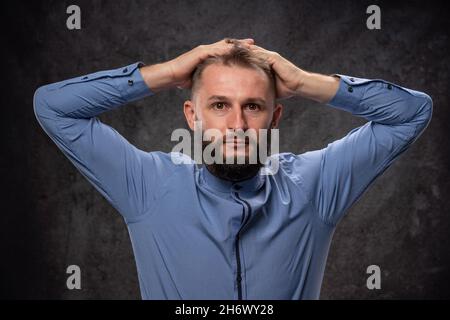 Ein junger Mann, der mit den Händen den Kopf hielt, war emotional schockiert und verängstigt. Auf einem dunklen texturierten Hintergrund im Studio. Stockfoto