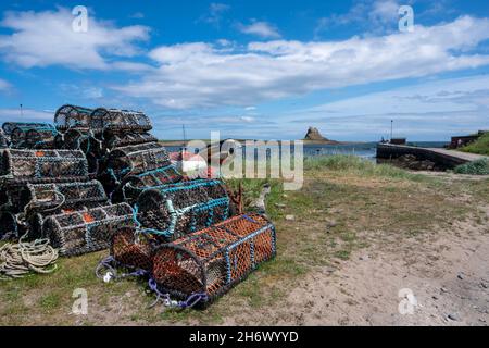 Lindisfarne Harbour, Holy Island, mit dem alten Schloss im Hintergrund und einer Reihe von Hummertöpfen und Booten. Stockfoto