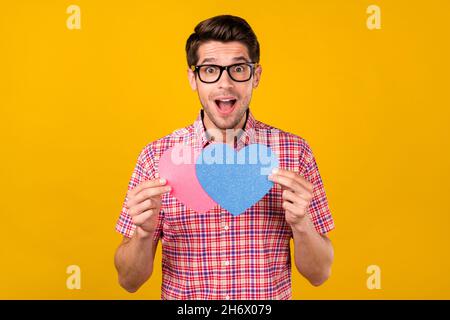 Portrait von attraktiven erstaunt fröhlich Kerl hält immer zusammen zwei Herz Zeichen amour isoliert über hellen gelben Hintergrund Stockfoto
