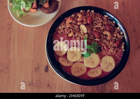 Draufsicht auf eine gesunde vegane Smoothie-Schale aus roter Drachenfrucht, Bananen mit Hafer Cashewnüssen und Mandeln Stockfoto