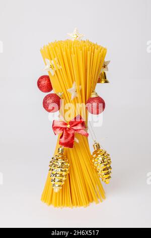 Ein Bouquet aus rohen Spaghetti in Form eines Weihnachtsbaums mit Spielzeug, roten Kugeln und Tannenzapfen. Weihnachtsbaum aus Lebensmitteln. Italienisches Essen. Stockfoto