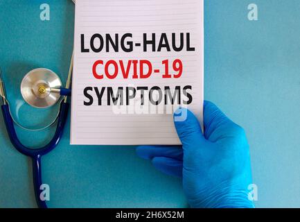 COVID-19 Symbol für langstreckige kovide Symptome. Weiße Karte mit Worten Langstrecke covid-19 Symptome. Arzthand, Stethoskop, blauer Hintergrund, Kopierraum. Ich Stockfoto
