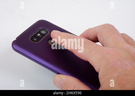 Jemand bringt einen Finger zum Fingerabdrucksensor auf dem Smartphone auf der Rückseite des Smartphones Stockfoto